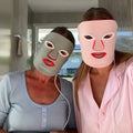 Two people wearing the NursesChoice Couples Edit LED masks lit up, in sage and blush pink
