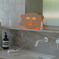 NursesChoice LED face mask lit on a bathroom vanity beside the Hyaluronic Acid Serum, stocked by Nurse Lisa at The Glow Co. Aesthetics, Gordon Park Brisbane